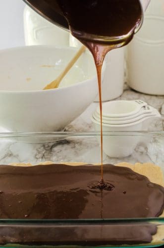 melted chocolate layer being poured over baked peanut butter fudge bars crust.