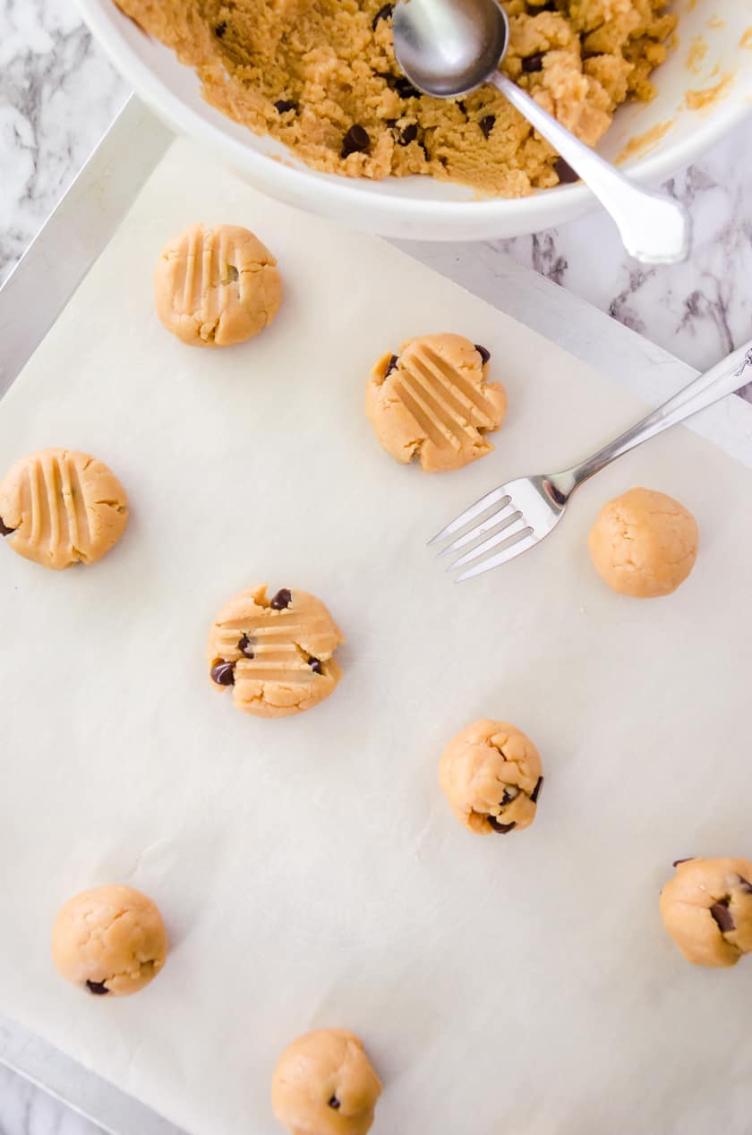 Simple peanut butter chocolate chip cookie dough balls on a cookie sheet and flattened with a fork