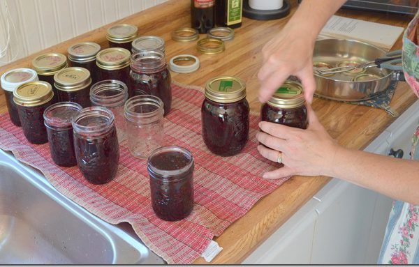 a woman twisting on the lid to a homemade jar of blackberry jam