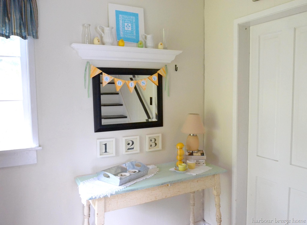 An entryway table with a mirror hung above it. A yellow paper bunting banner is hanging at the top of the mirror with letters that spell "shine" on it.