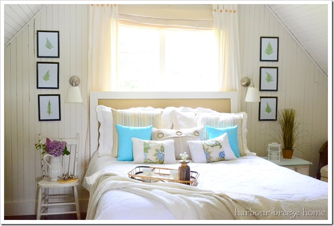 A cottage style bedroom with three fern leaf printings hung on either side of the bed on creamy white walls.