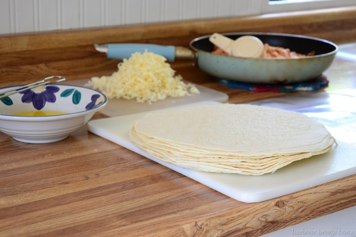 A stack of tortillas on the counter with a pan of cheese and stack of grated cheese behind it.