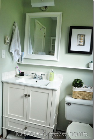 New bathroom vanity with small square tiles as backsplash and a white mirror above it with a shelf underneath