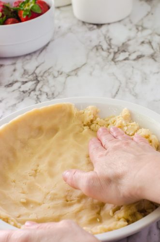 Pie crust being patted into a pie pan