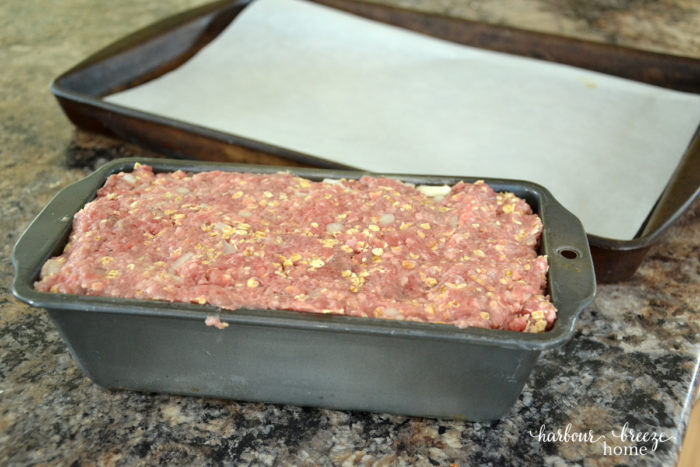 Meatloaf mixture pressed into a loaf pan with a large parchment paper lined pan beside it.