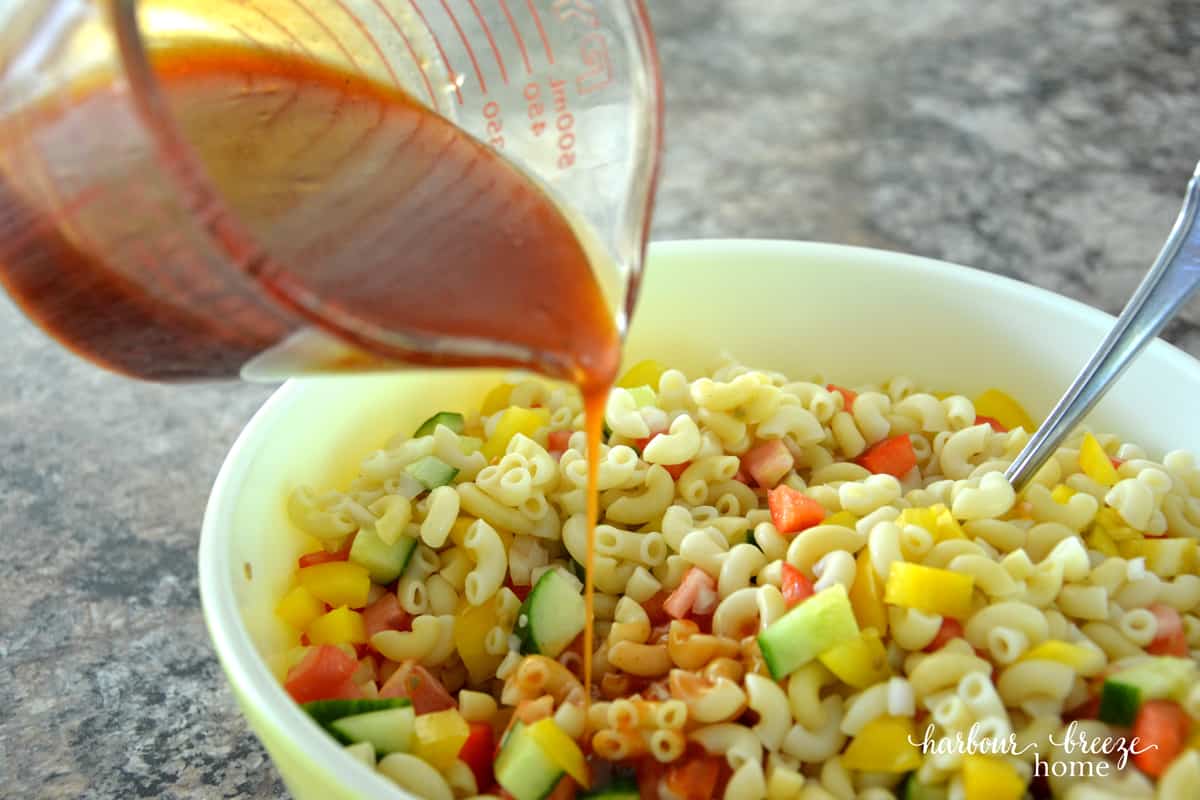 Macaroni Salad in a vintage pyrex bowl with dressing being poured over it