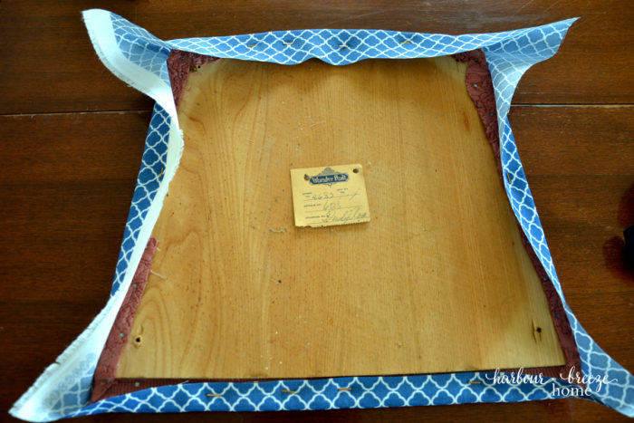 New fabric stapled to the underside of a dining chair cushion. The sides are stapled first and then the corners.