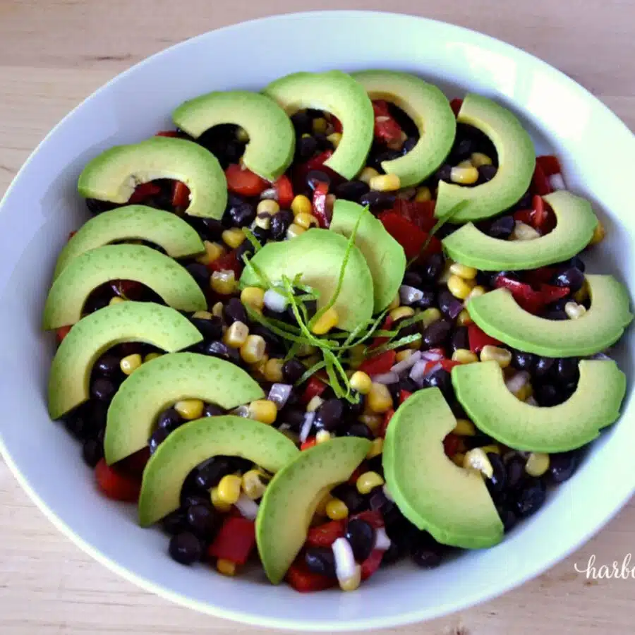 a bowl of black bean salad garnished with sliced avocados and lime zest