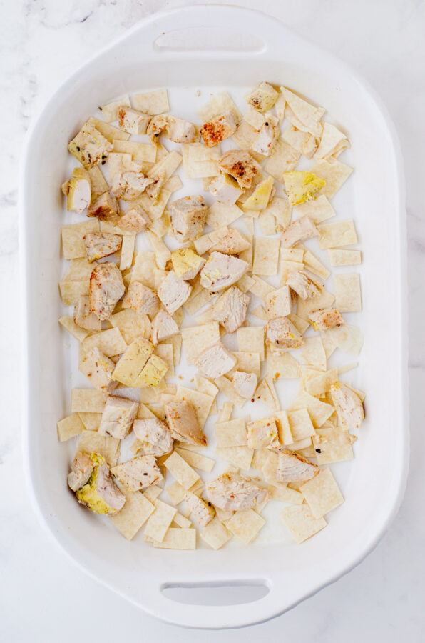 Diced cooked chicken layered over cut up flour tortillas in a baking dish for Mexican Chicken Casserole