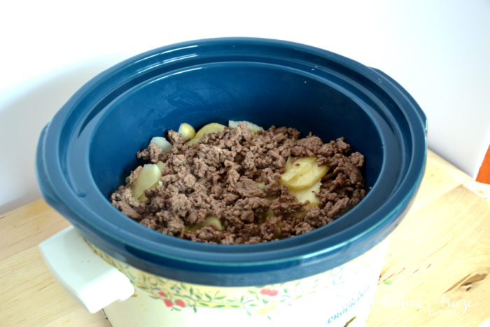 browned ground beef layered on top of potatoes in crock pot