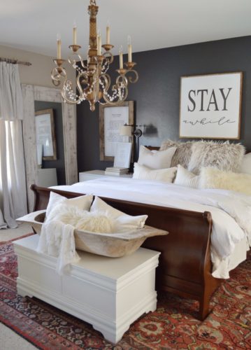 A farmhouse style bedroom with a black feature wall with a bed with a wooden frame against it with white bedding.