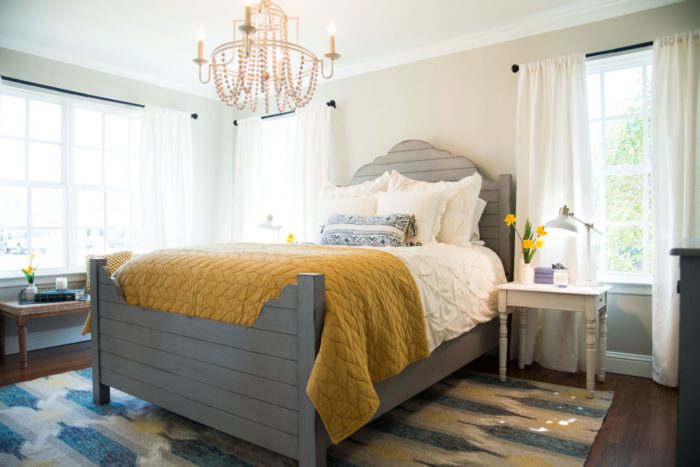 A gray headboard made out of wood planks on a gray bed with white and mustard yellow linens