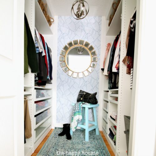 A small closet organized with the IKEA pax wardrobe system on the left and right sides of the room with wallpaper and a mirror straight ahead.