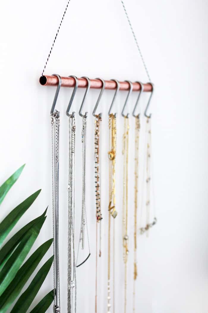 Rope strung through a copper pipe and hung on the wall becomes a beautiful organizer for necklaces when s- hooks are hung over it.