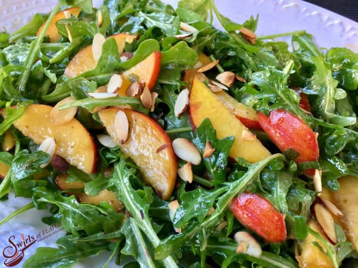 Salad greens with grilled peaches and almond slices on a white plate