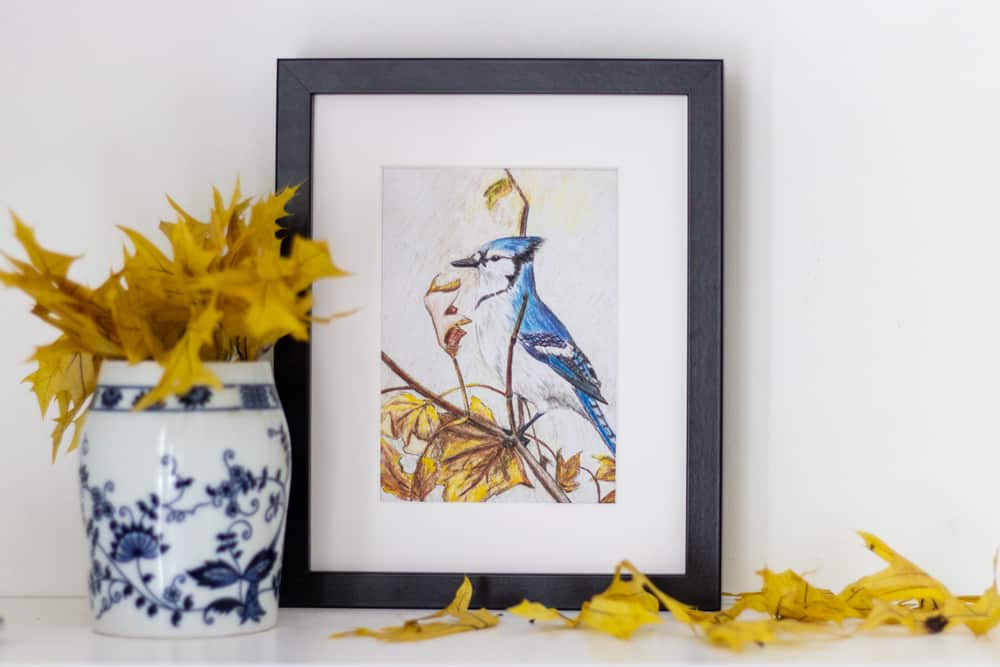 a blue bird art print with a vase of yellow leaves in front of it