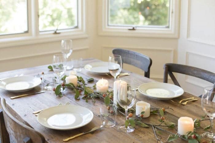 a simple fall tablescape with a wood table, white plates, and simple branches and candles as the centerpiece
