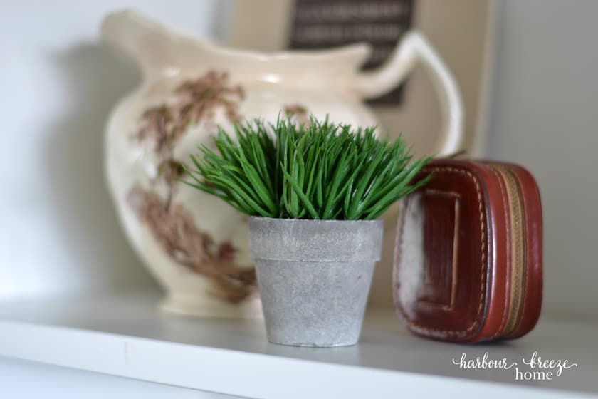 small pot of fake greenery beside an old antique pitcher for a farmhouse bookshelf decor idea