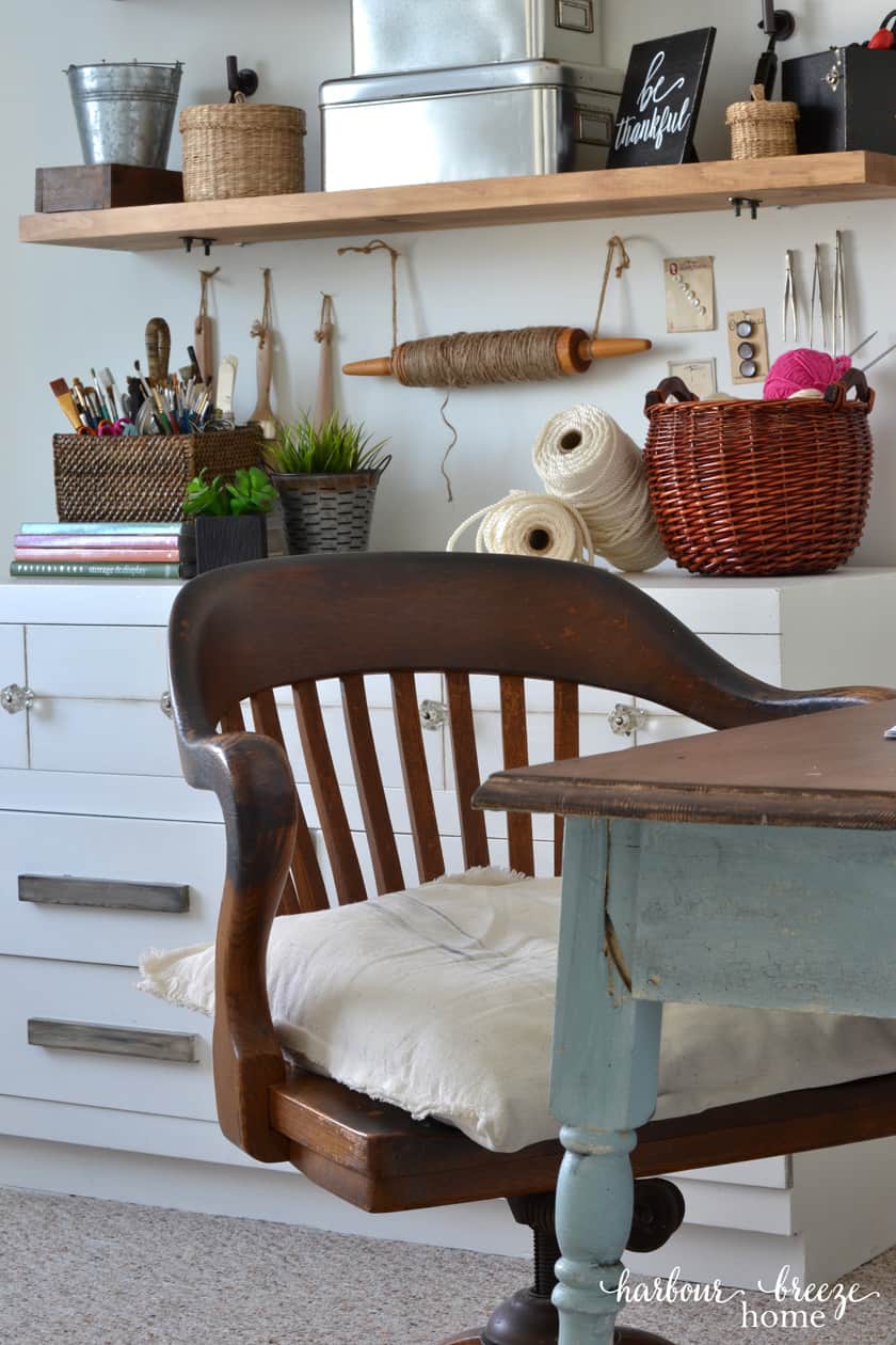 Antique Wooden Desk Chair at a farmhouse table with a wall of shelves with craft supplies in the background.