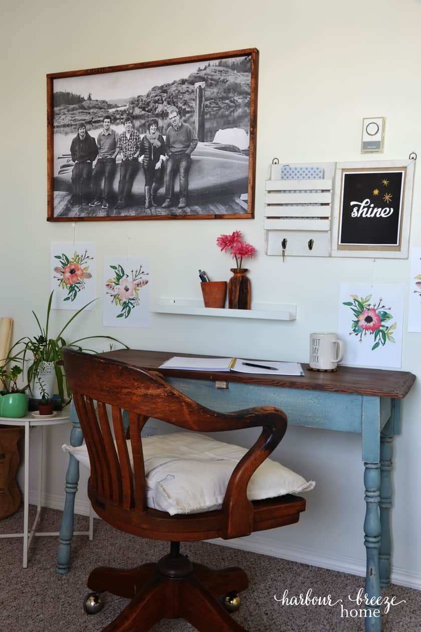 Farmhouse Table with Antique Desk Chair sitting at it with greenery beside and pictures of pink flowers on the wall.