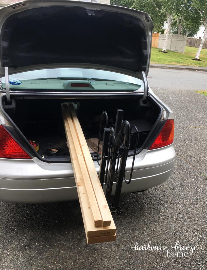 Trunk of car with boards hanging out the back for DIY floating shelves.
