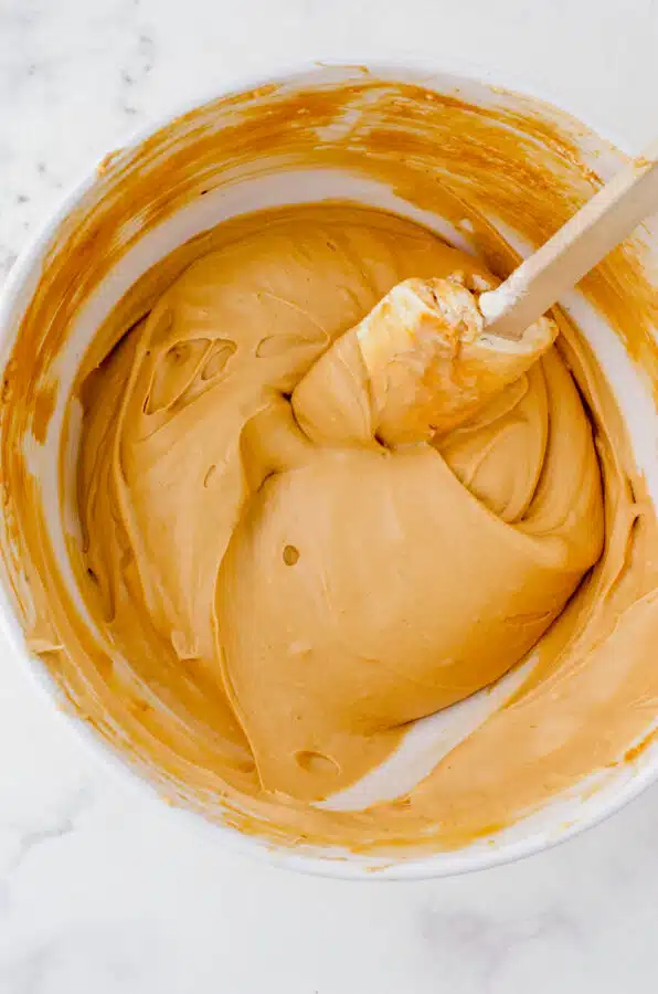 Whipping cream folded into coffee flavored marshmallows in a bowl.