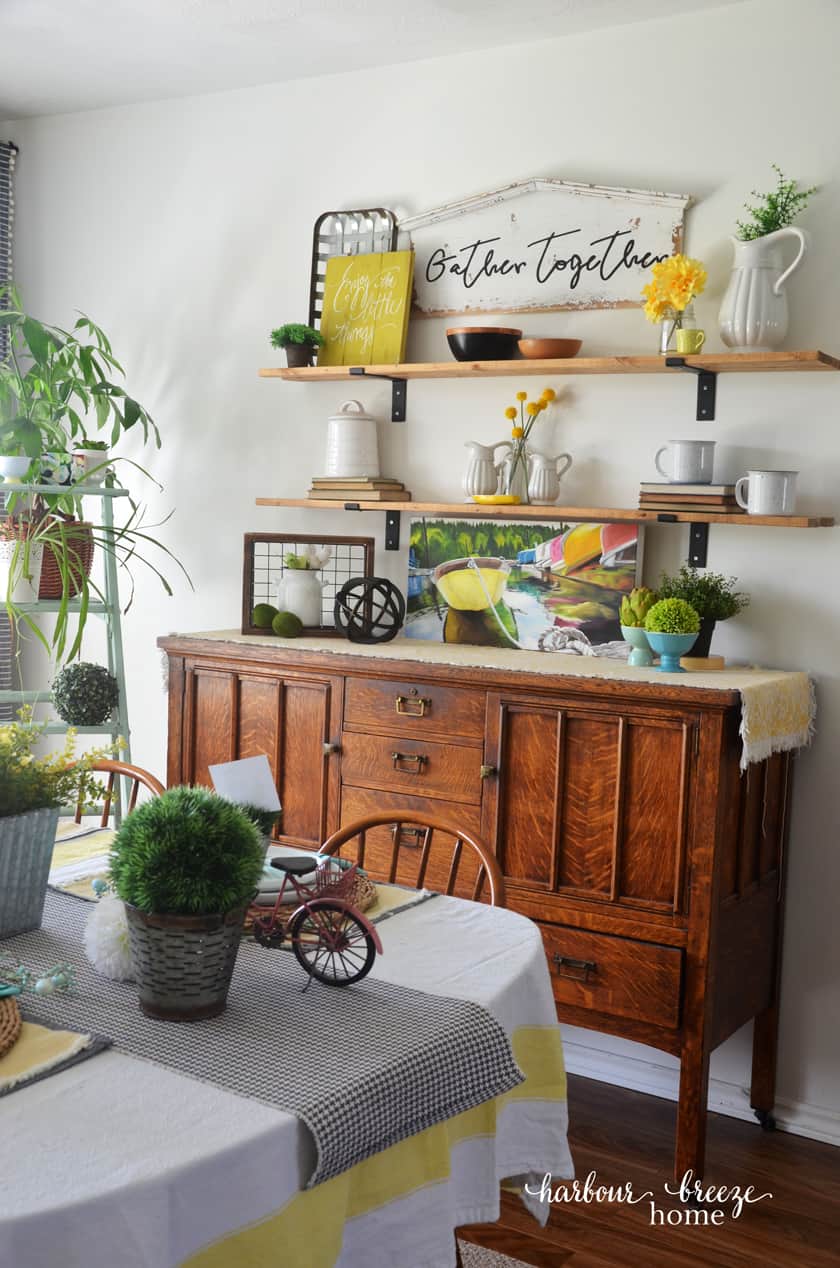 dining room decor on shelves above buffet featuring whites and yellows with real and faux plants