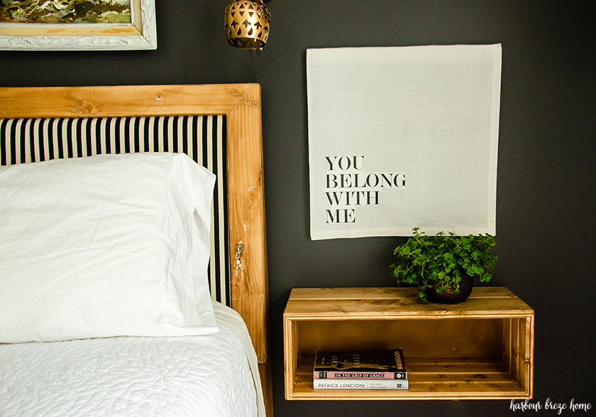 The floating bedside table completed and hung on the wall beside a bed with a plant on the top and books in the shelf.
