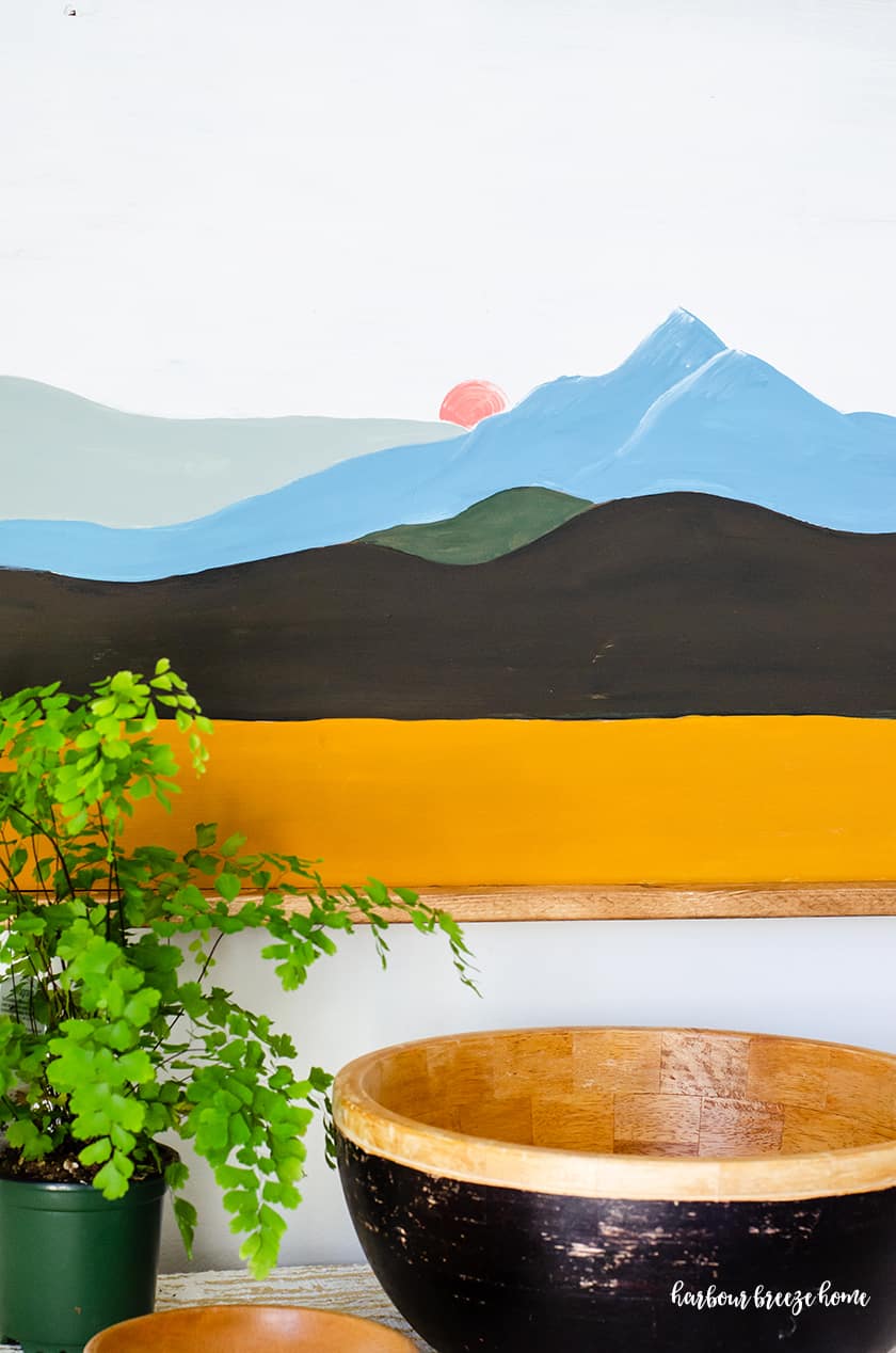 An easy mountain painting with color blocked lines with the colors yellow, black, green, blue and gray - with a pink moon peeking behind the mountain