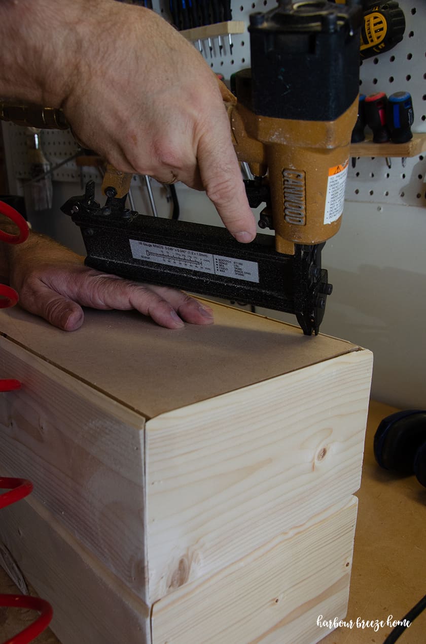 The back piece of wood being attached to the back of a floating bedside table with a brad nailer.