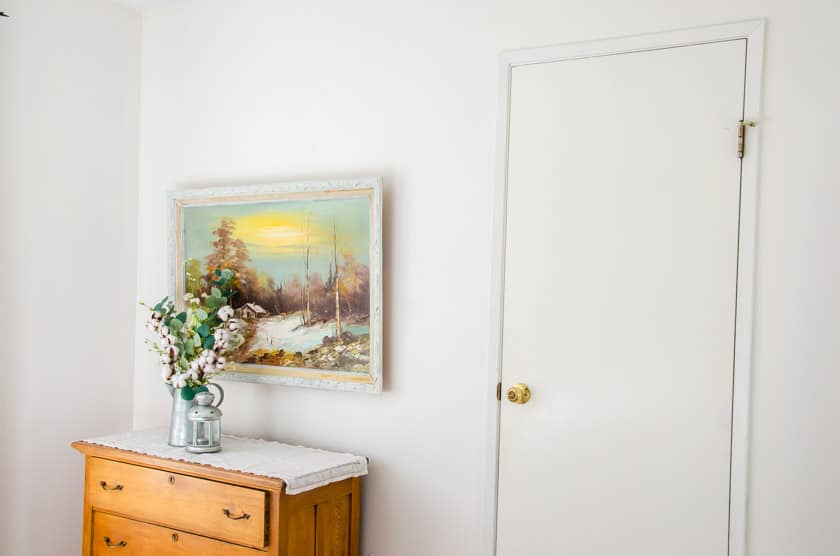 A plain looking wall with a dresser with art above it.
