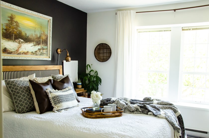 Master bedroom with a bed against a dark painted wall and light colored wall with window beside it.