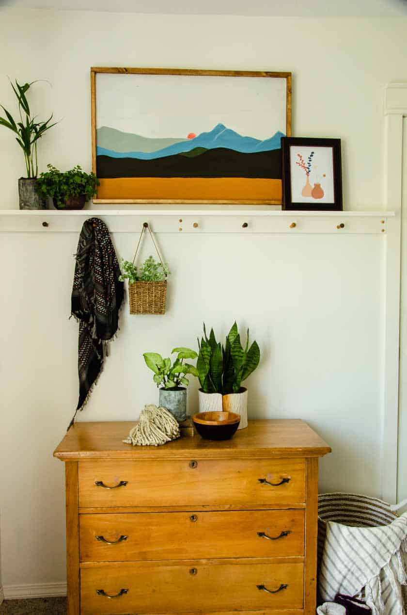 A Boho shelf with pegs with boho art above and plants on the shelf