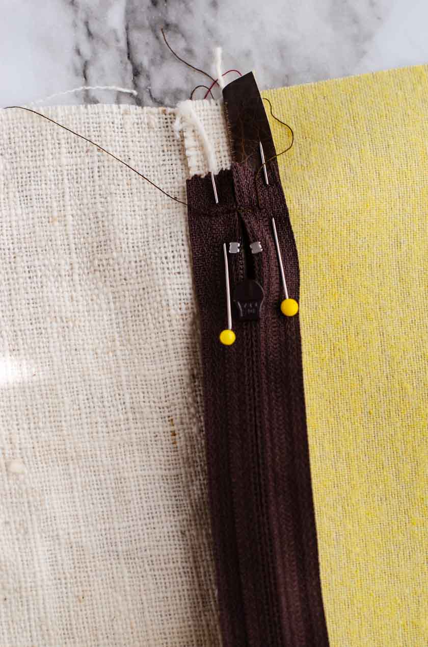Pins holding a zipper facedown on top of the bottom seam of a faux leather pillow cover.