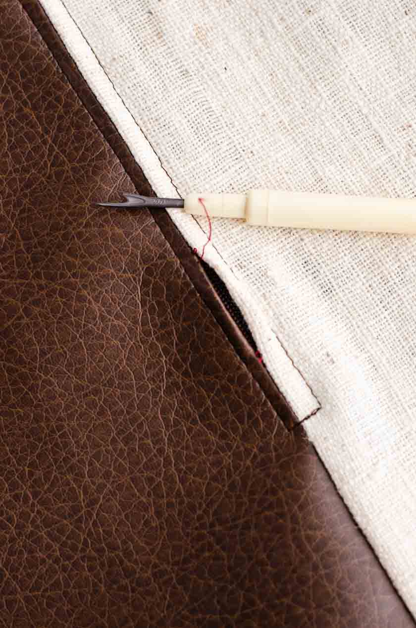 Pulling the seam out to reveal the zipper on a faux leather pillow cover.