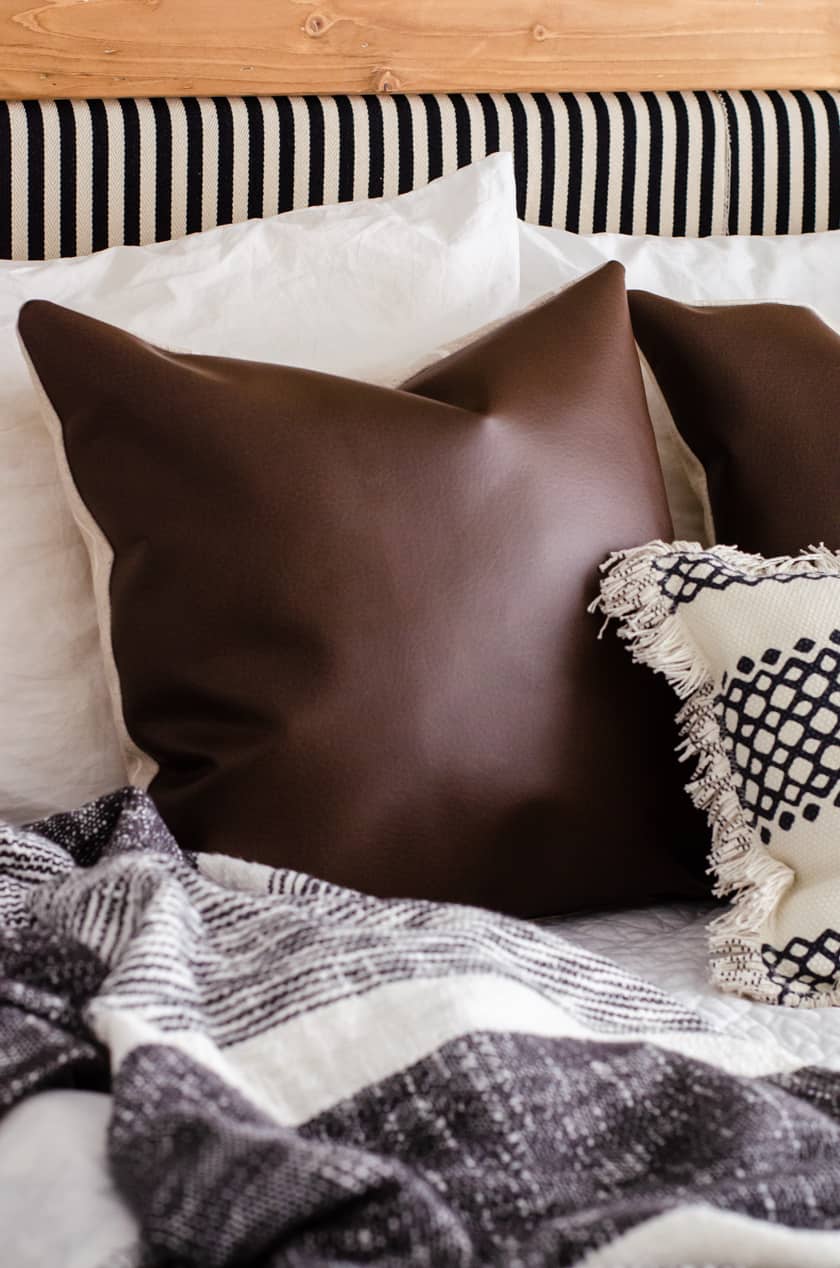 A faux leather pillow cover with a pillow insert displayed on a bed.