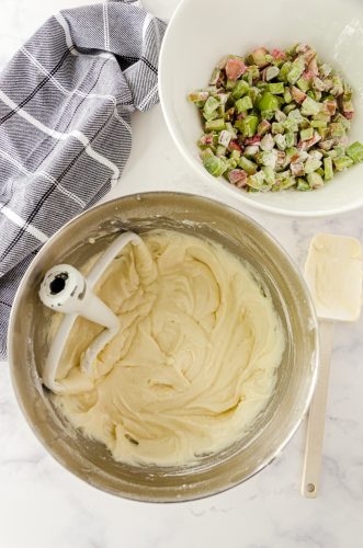 Rhubarb coffee cake batter mixed in the bowl of a stand mixer with flour covered rhubarb in another bowl.