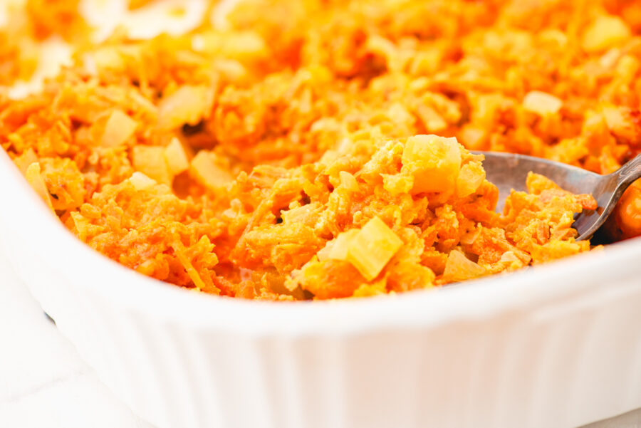 A casserole dish of shredded carrot casserole with a serving spoon in it.