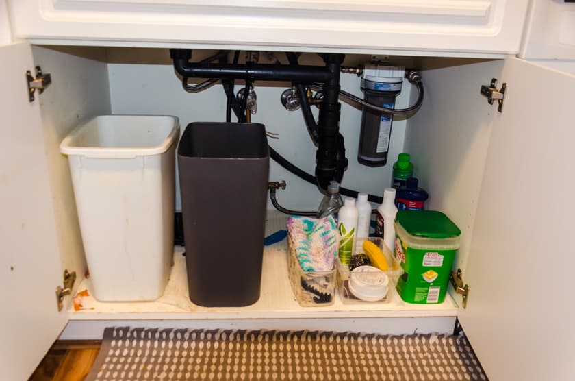 A dirty cupboard that needs organizing under the kitchen sink.