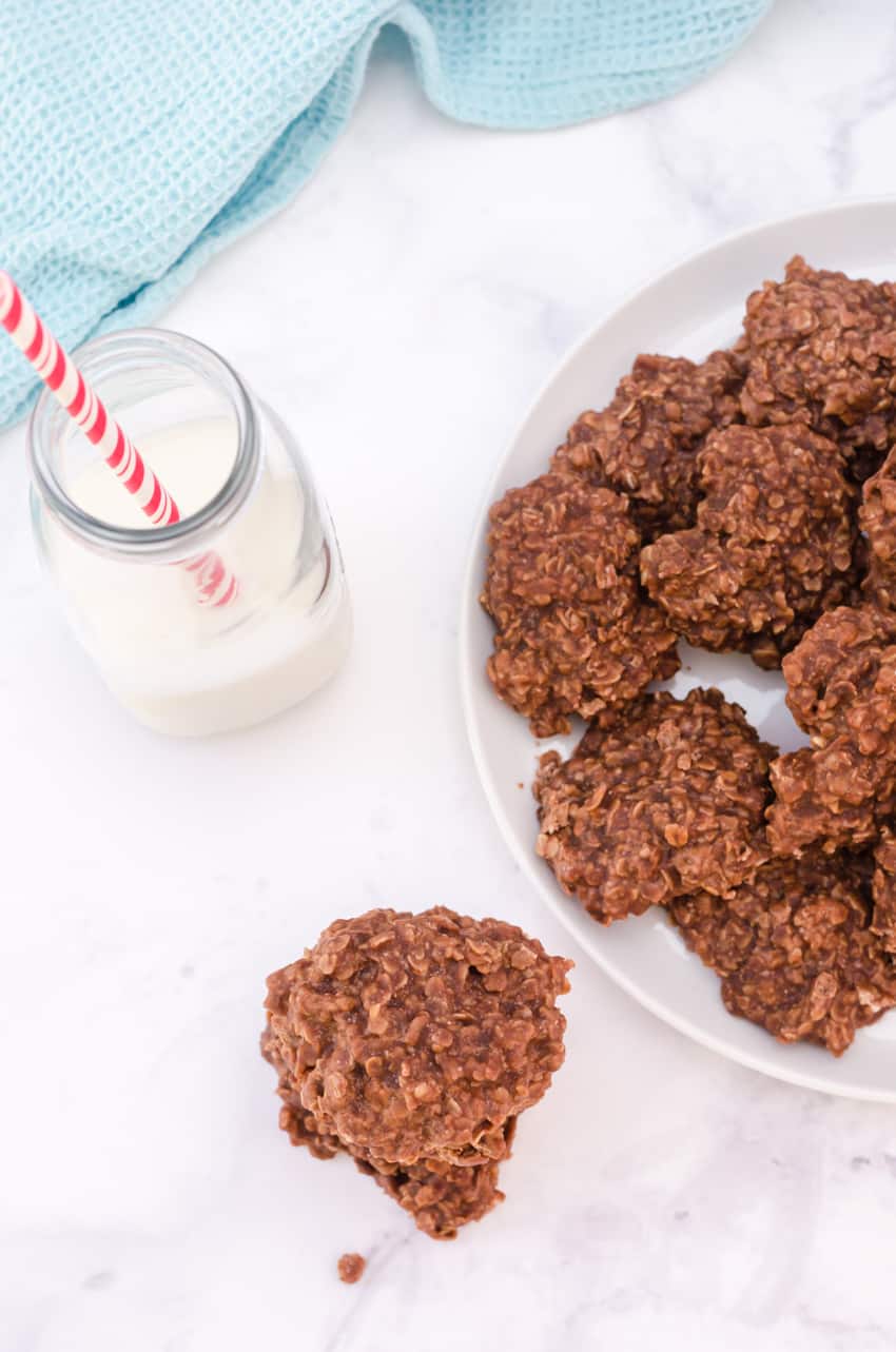 No bake cookies with oatmeal and chocolate on a plate with a glass of milk beside.