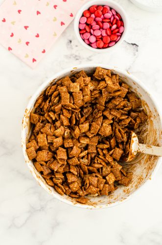 Chocolate mixture being stirred into chex mix cereal for puppy chow snack mix.