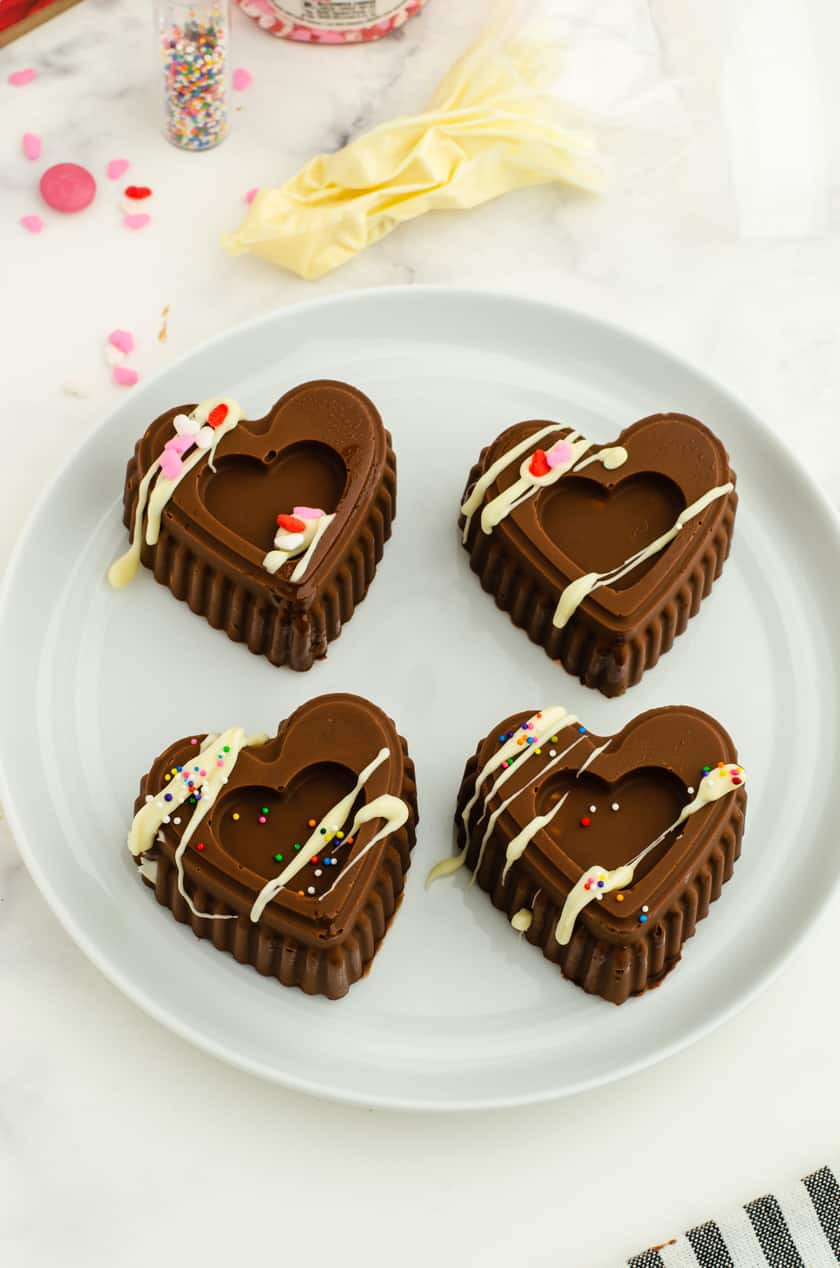 four valentines hot cocoa bombs on a plate decorated with drizzles of white chocolate