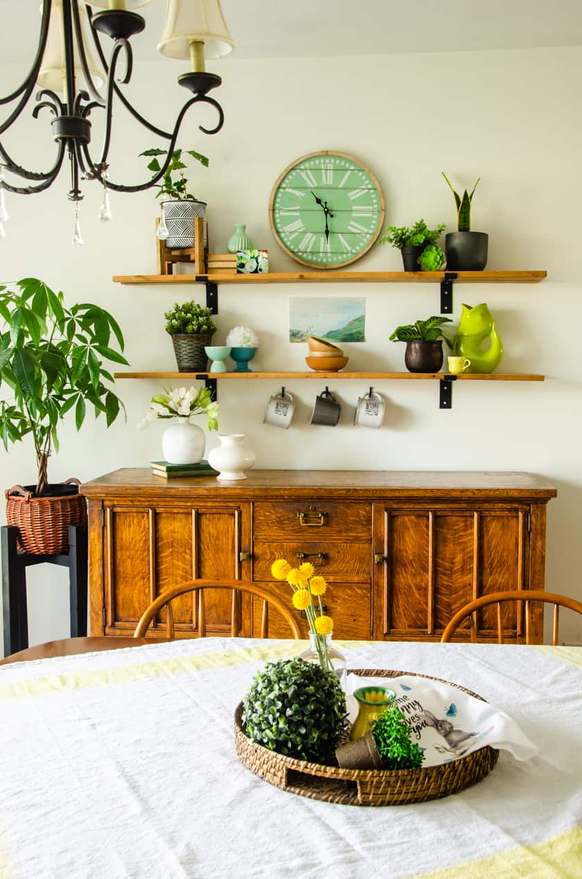 Antique oak dining room buffet with two farmhouse shelves above it with faux and real houseplants arranged on it.