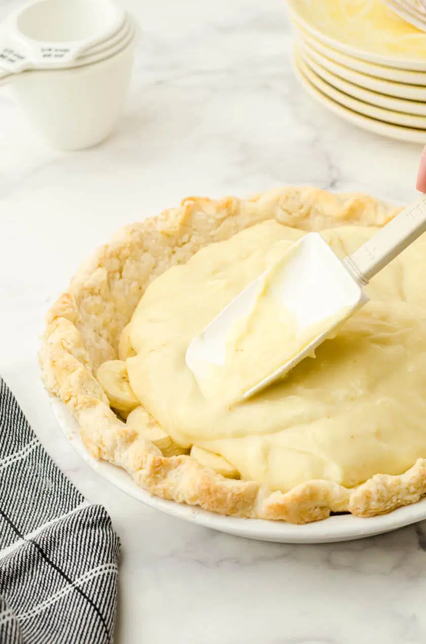 Vanilla pudding being spread over bananas in a banana cream pie shell