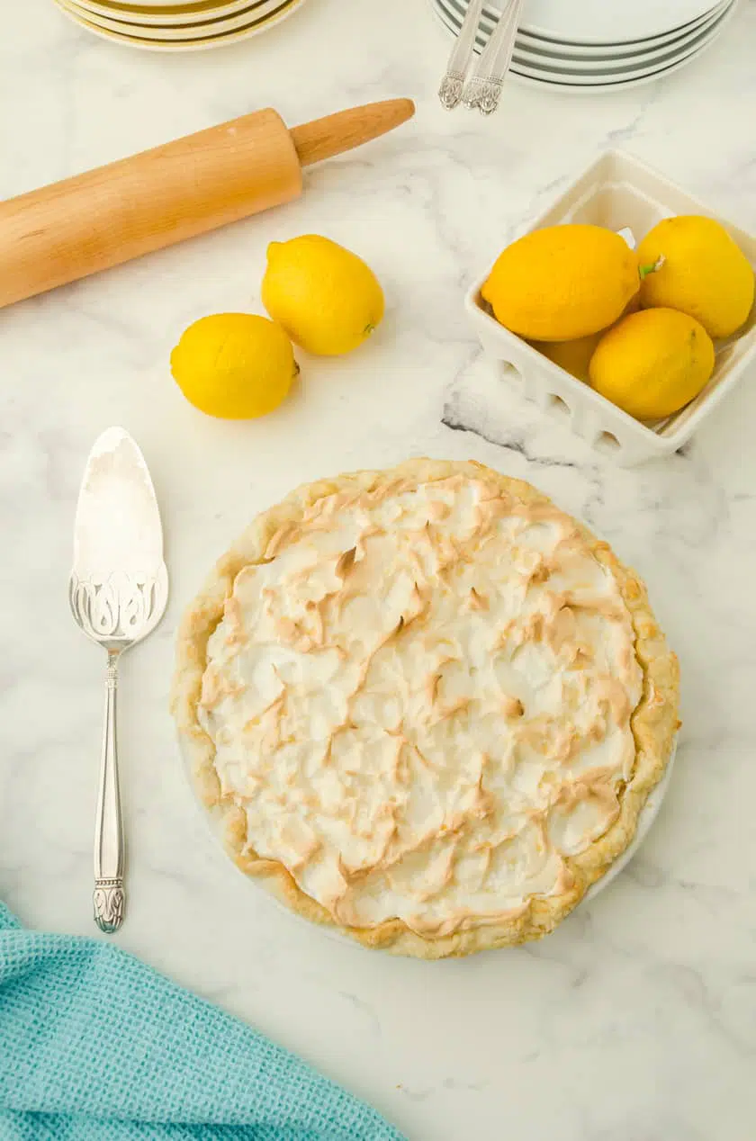 A whole lemon meringue pie with a basket of lemons beside.