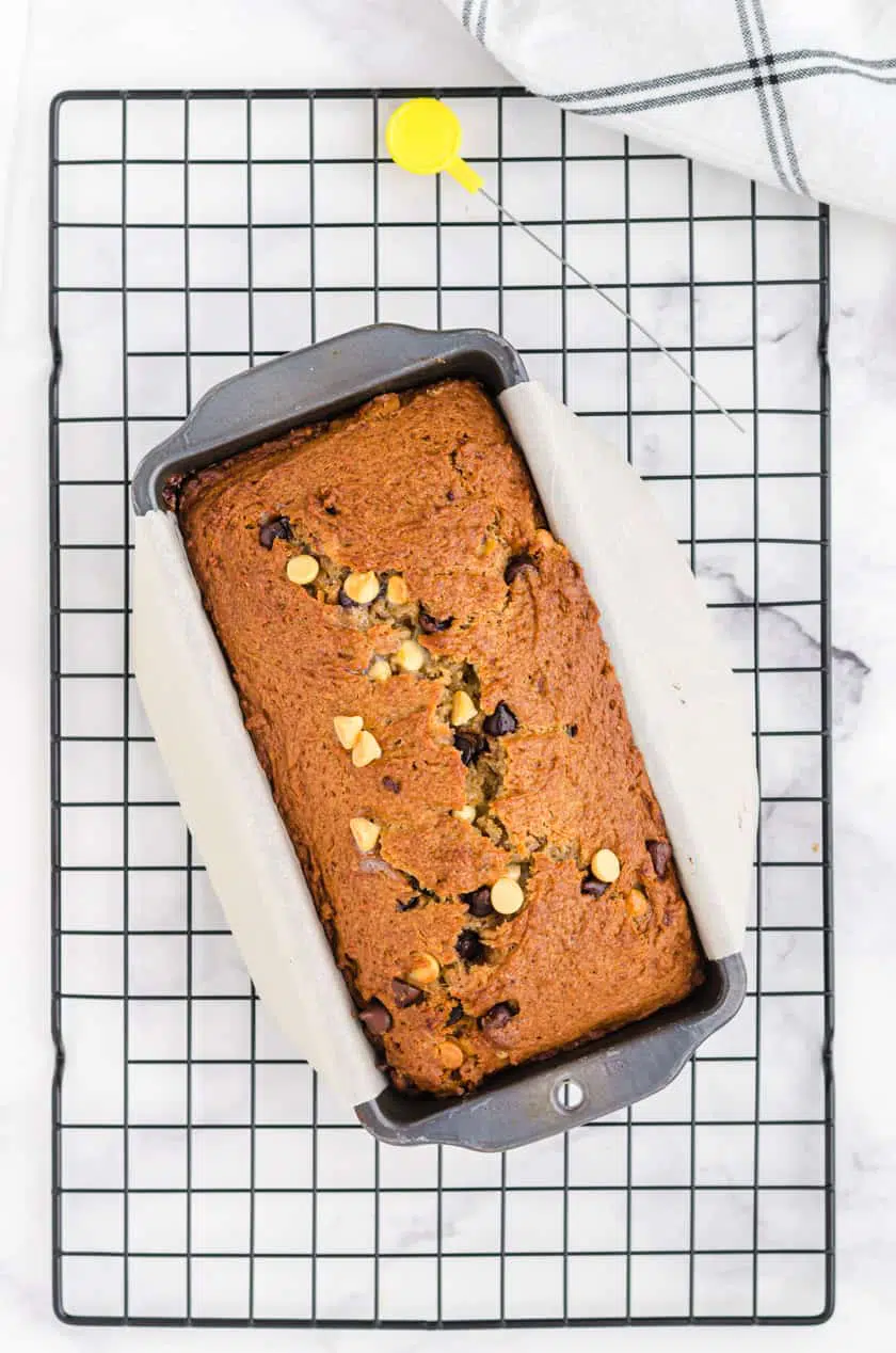 Peanut Butter Chocolate Chip banana bread in a loaf pan sitting on a cooling rack.