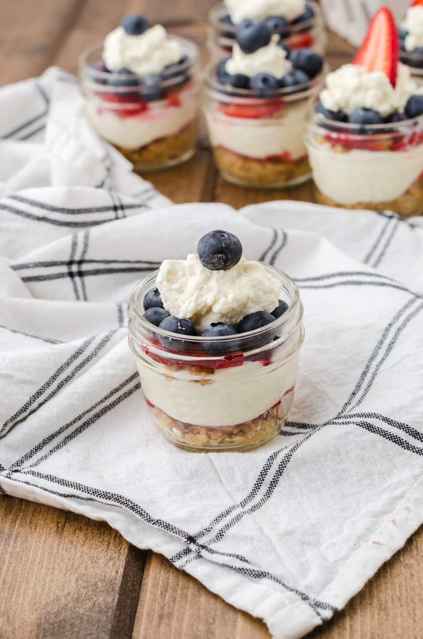 A mason jar filled with layered no bake cheesecake with a blueberry on top.