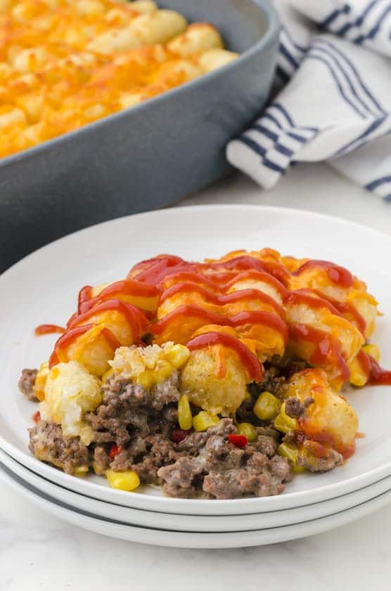 Tator tot casserole dished out on a plate with ketchup drizzled on the top.