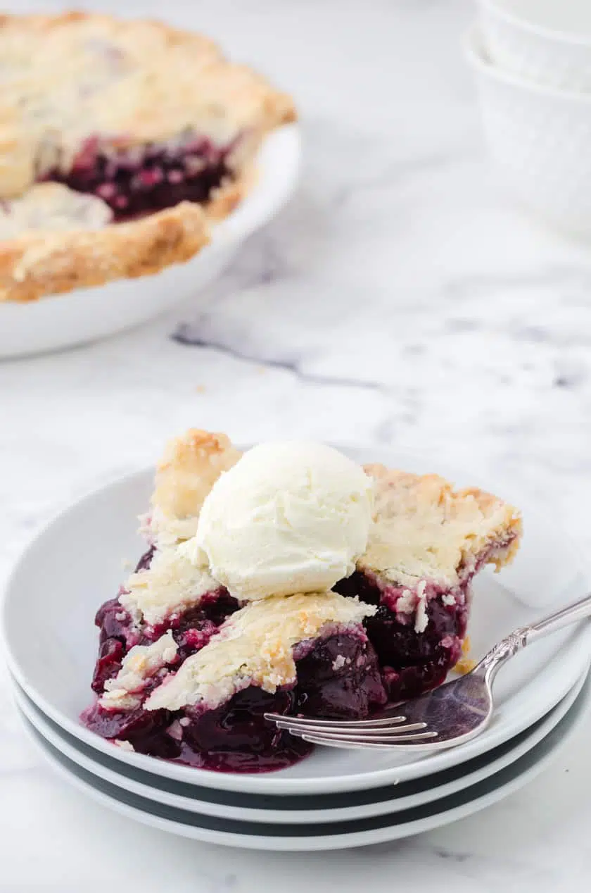 A slice of homemade cherry pie made with canned cherries with a scoop of ice cream on it.