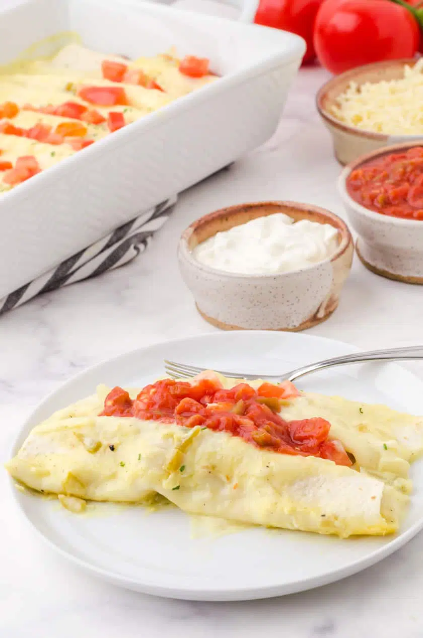 A plate with 2 chicken enchiladas on it with salsa and sour cream on the top.